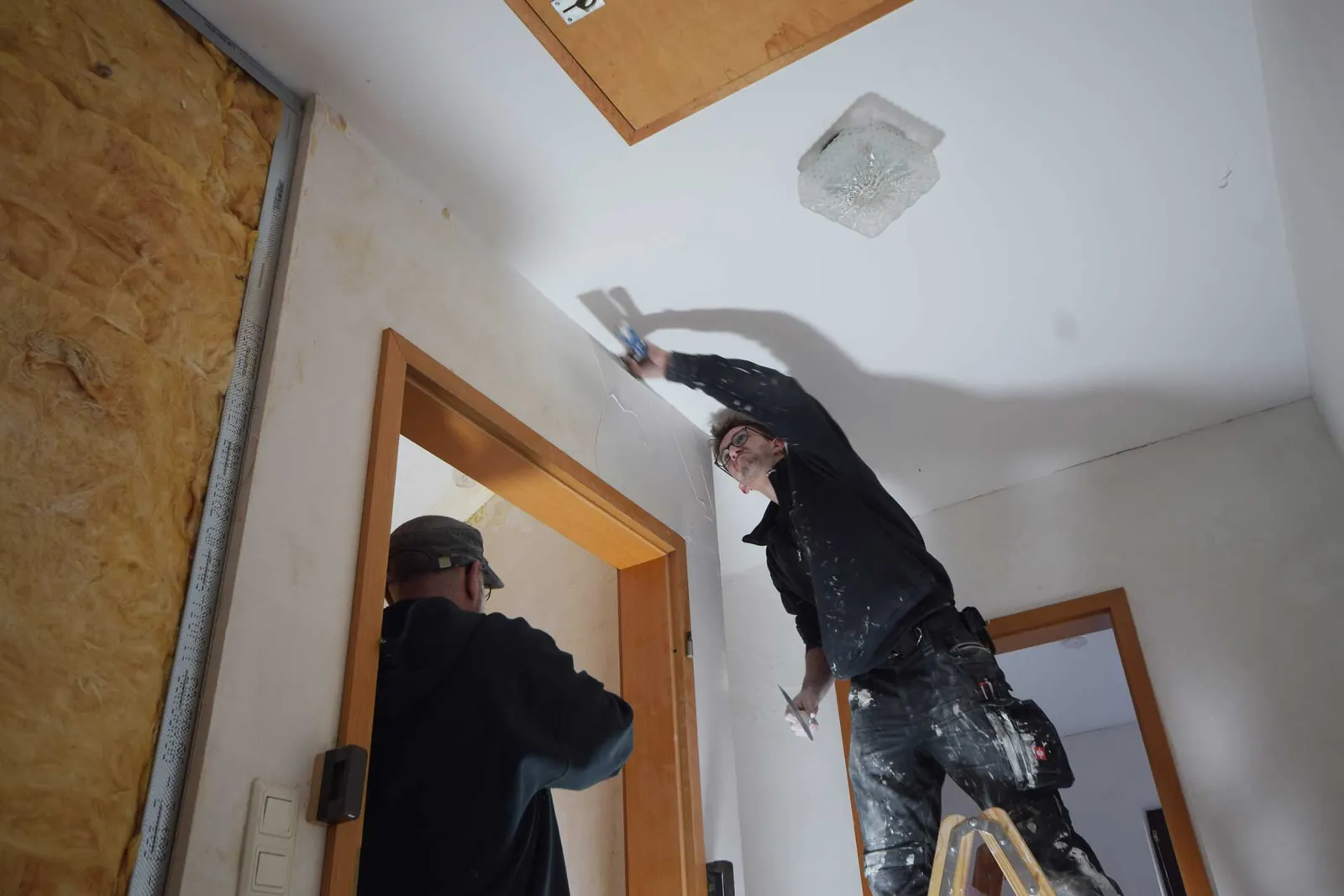 Mitarbeiter bei Deckenarbeiten auf einer Leiter neben einer Trockenbauwand